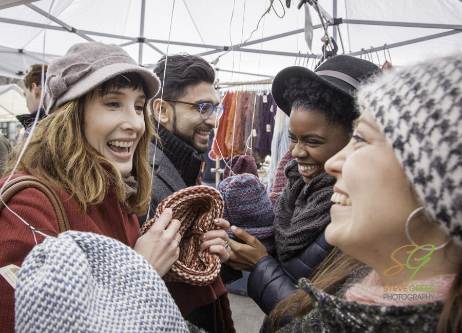 Mixed Race Group having fun shopping for winter hats in outdoor city market.
